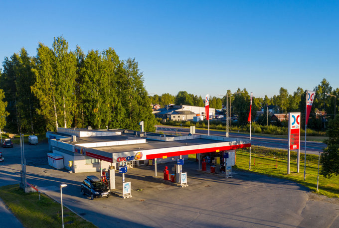 Ett drönarfoto över en OKQ8 station på Klemensnäs i Skellefteå med bil som tankar, i bakgrunden syns träd, en väg och bebyggelse